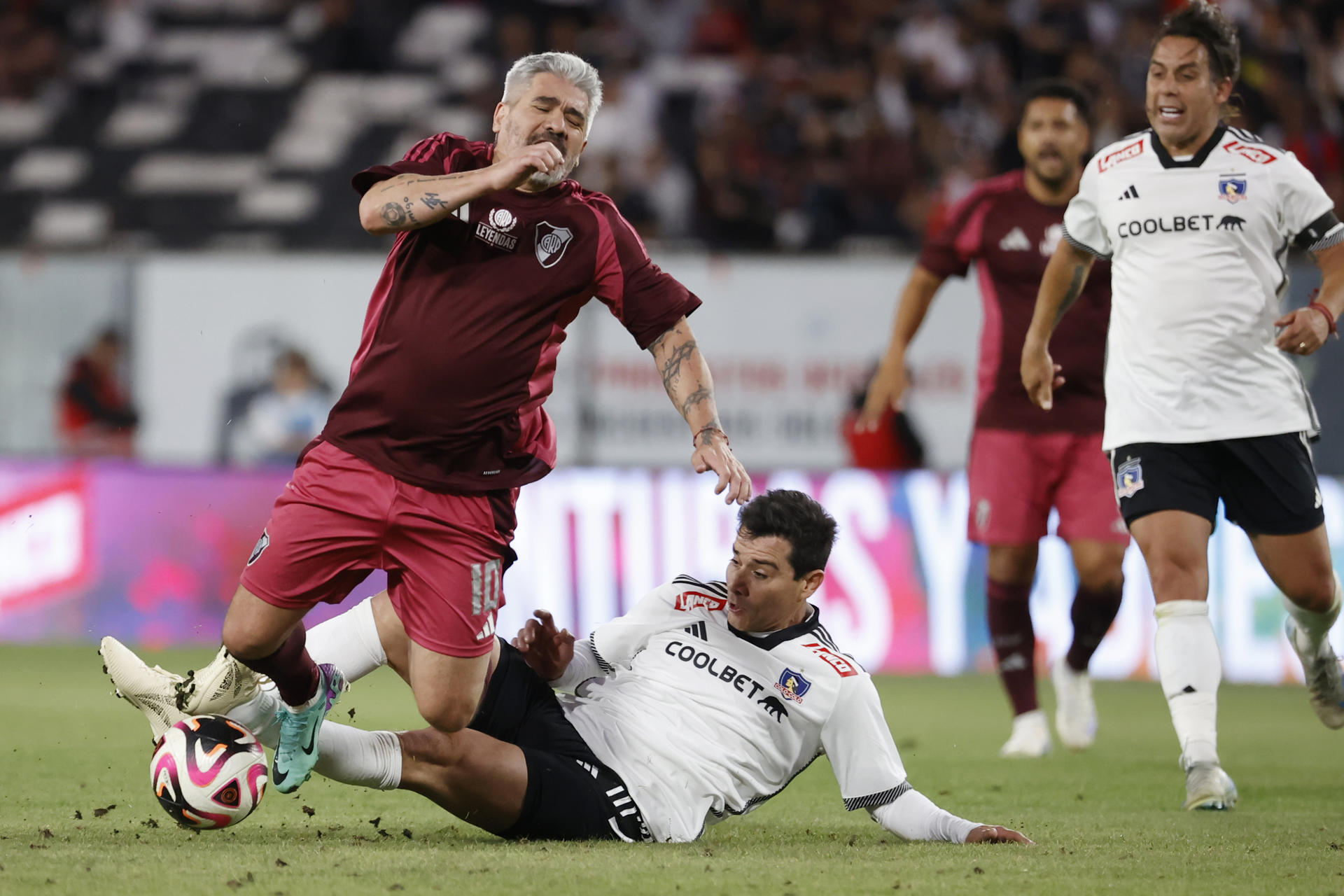 El excreativo argentino Ariel Ortega recibe una falta del exdefensor chileno David Henriquez (abajo) durante el partido de leyendas del fútbol que enfrentó este sábado a dos equipos especiales de Colo Colo y River Plate en el estadio Monumental, de Santiago. EFE/Elvis González
