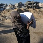 Una mujer palestina lleva un saco de harina después de recibir ayuda alimentaria en un centro de distribución del organismo de las Naciones Unidas para los Refugiados en Khan Younis, en la Franja de Gaza. EFE/ Haitham Imad