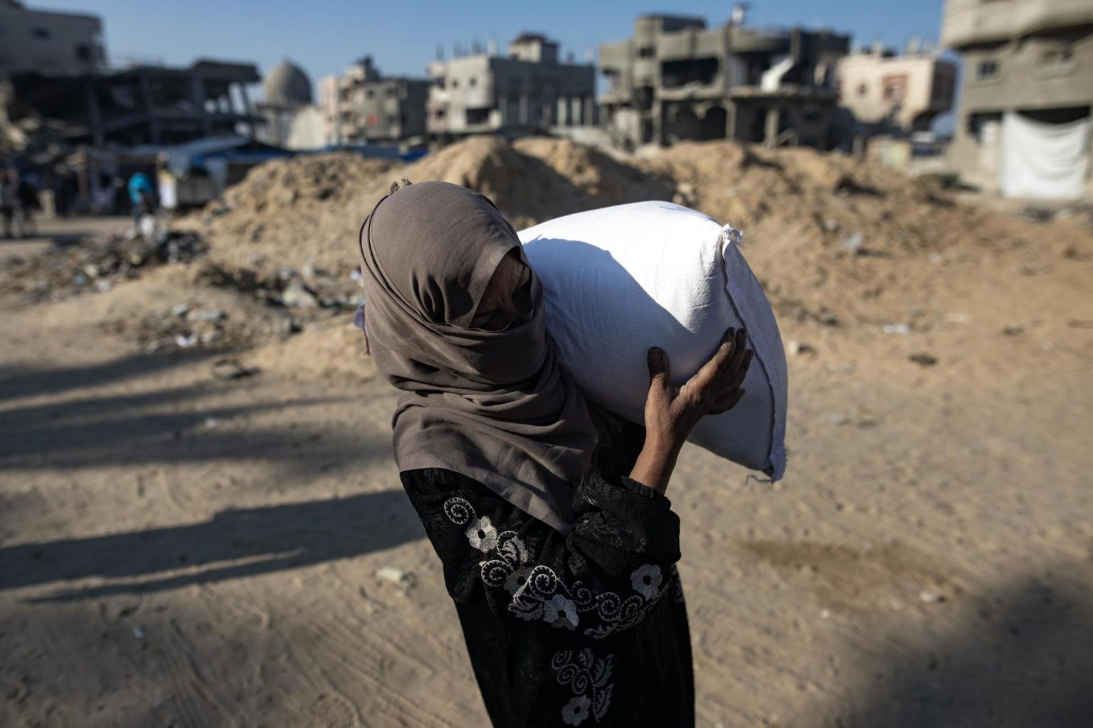 Una mujer palestina lleva un saco de harina después de recibir ayuda alimentaria en un centro de distribución del organismo de las Naciones Unidas para los Refugiados en Khan Younis, en la Franja de Gaza. EFE/ Haitham Imad