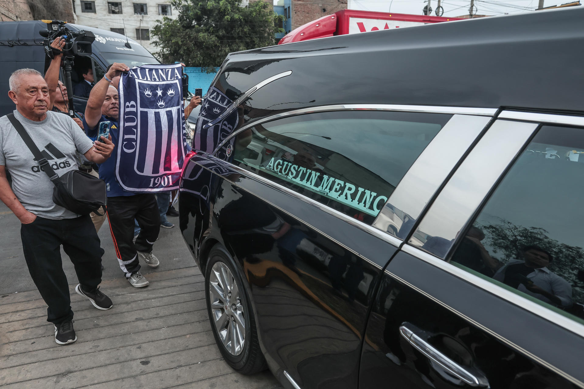 Aficionados acompañan este lunes el vehículo que transporta el féretro del exfutbolista peruano Hugo 'el Cholo' Sotil hacia el estadio del club Alianza Lima. EFE/ Aldair Mejía
