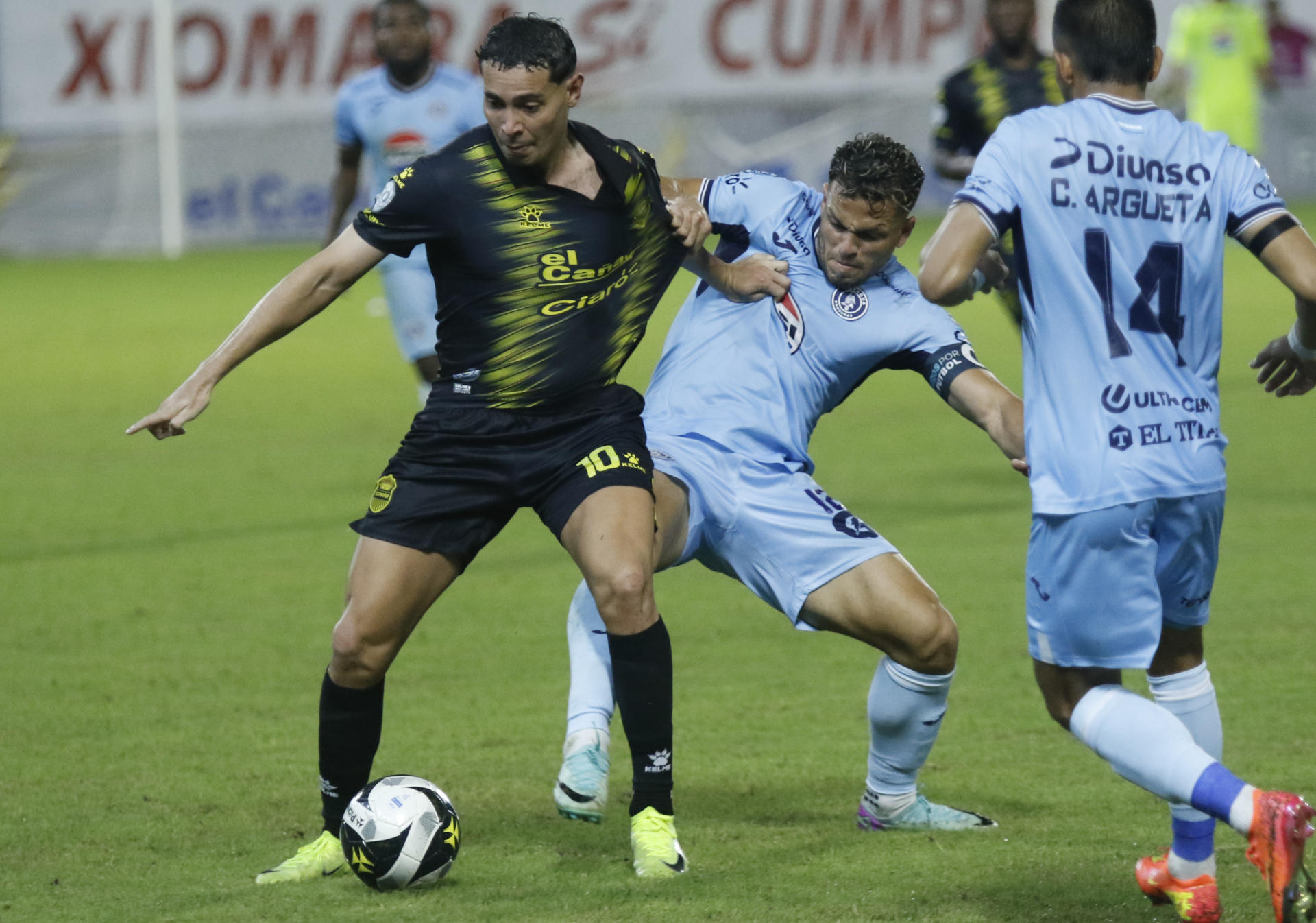 Marcelo Santos (c) de Motagua disputa el balón con Jhow Benavides del Real España, este jueves durante el partido de ida de las semifinales del torneo Apertura hondureño jugado en el Estadio Francisco Morazán, en San Pedro Sula. EFE/ José Valle
