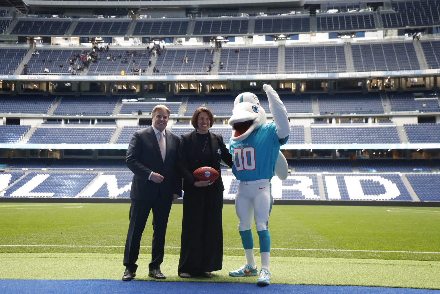 Brett Gosper, director de la NFL en Europa y Asia-Pacífico y Pri Shumate, vicepresidenta de los Miami Dolphins, en el césped del Santiago Bernabéu con la mascota del equipo, durante el acto celebrado este viernes. EFE/ Blanca Millez