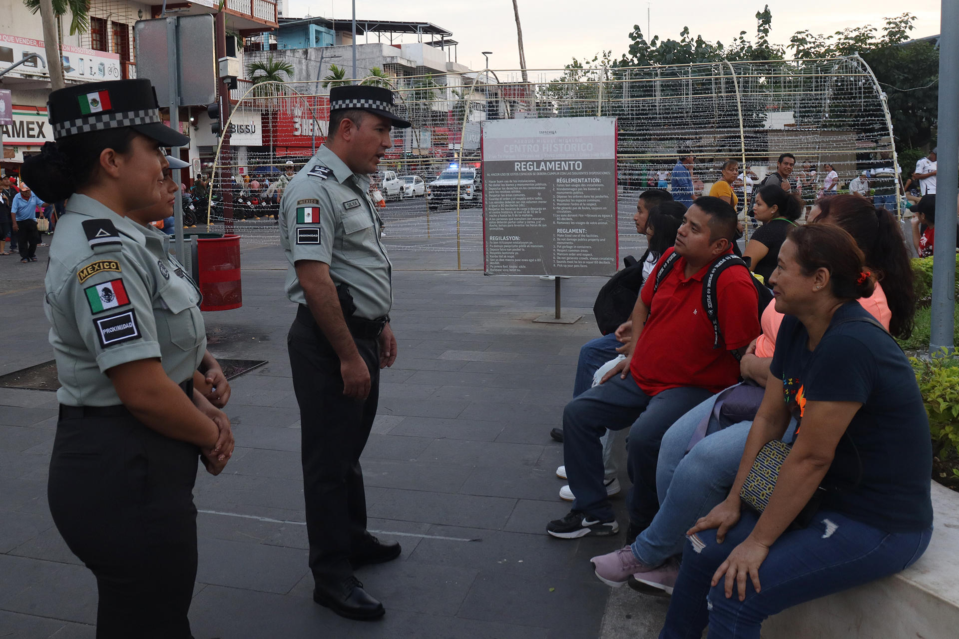 El primer subinspector del batallón 43 de la Guardia Nacional (GN), Luis Eduardo Silva Solís (c), y la oficial Dayana García Altamirano (i) dialogan con personas este jueves, en el municipio de Tapachula, en Chiapas (México). EFE/ Juan Manuel Blanco
