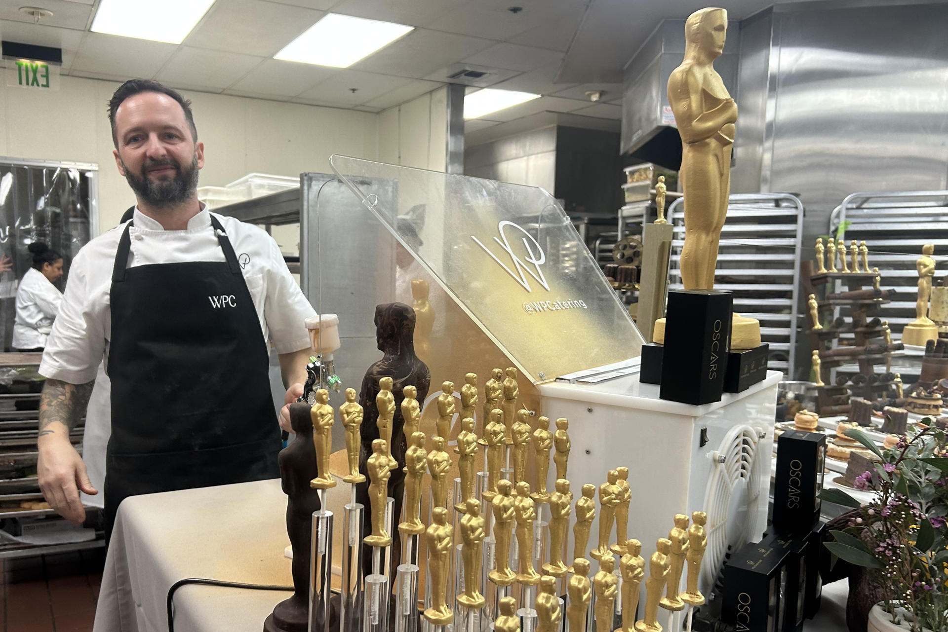 Un ayudante de cocina posa junto a figuras de chocolate de la estatuilla de los premios Oscar este jueves, en las cocinas del teatro Dolby en Los Ángeles (Estados Unidos). EFE/ Mikaela Viqueira
