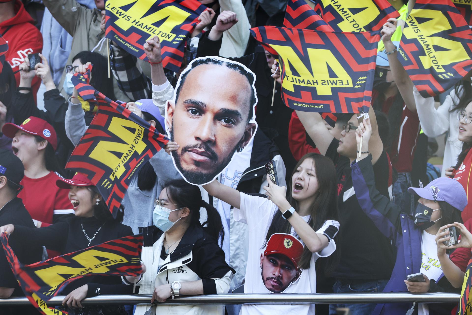 Seguidores de la escudería italiana Ferrari enarbolan banderas y un rostro del piloto británico Lewis Hamilton, quién se adjudicó este sábado la carrera al esprint del Gran Premio de China.EFE/EPA/WU HAO / POOL
